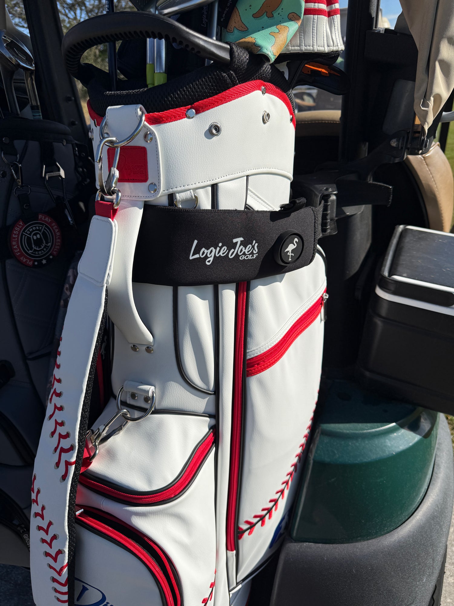 A White Magnetic Golf Cart Strap Sleeve (18.5 x 3.5 in, neoprene rubber) with dual accessory magnets, glove holder, and carabiner bag attachment is shown on a golf cart in the sun.