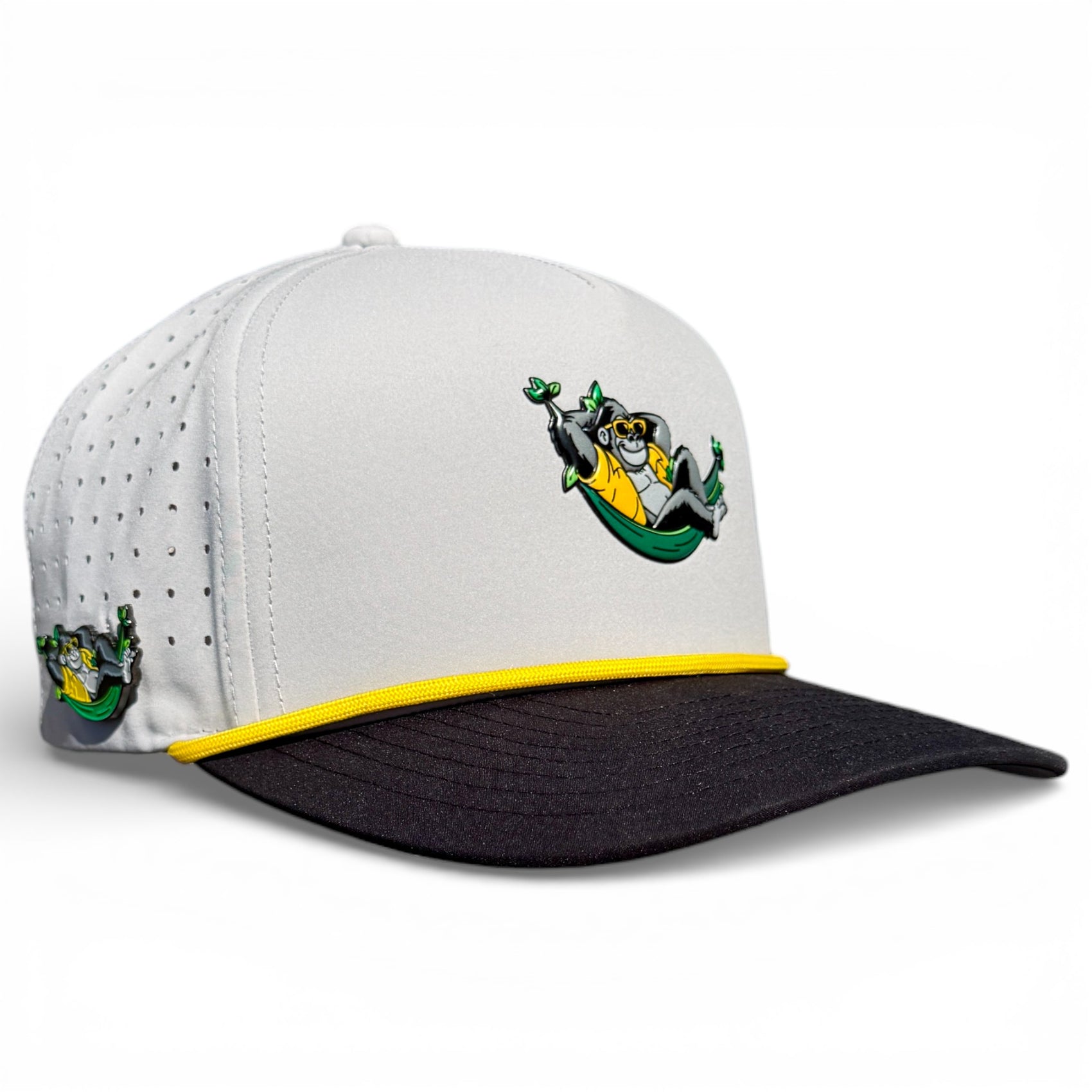 The Banana Hammock Golf Hat is a white and black snapback cap with yellow trim, featuring a cartoon monkey in a green banana hammock, plus a side logo, built-in magnetic ball marker holder (marker included), and adjustable fit.