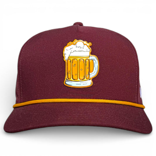 The Cold One Golf Hat is a maroon snapback cap with a yellow band and an embroidered beer mug, featuring a built-in magnetic ball marker holder with marker—adjustable and one size, perfect for fun on the golf course.