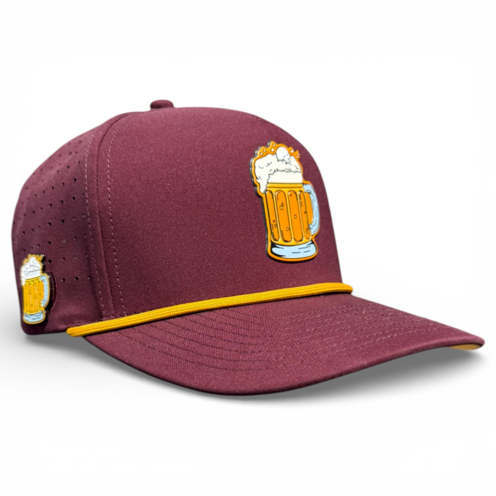 The Cold One Golf Hat is a maroon adjustable snapback cap with yellow trim, featuring an embroidered beer mug with foam on the front and side. It includes a built-in magnetic ball marker holder and marker, and is shown against a plain white background.