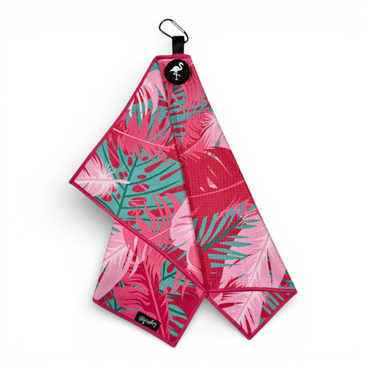 The Pink Tropical Golf Towel features a pink and teal palm leaf pattern and premium double-sided microfiber. Measuring 24 x 16 in, it includes a heavy-duty magnetic clip and carabiner for easy attachment, shown folded against a white background.