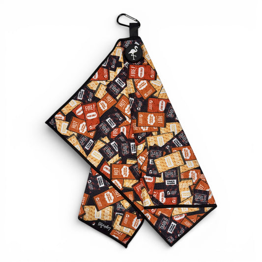 The Hot Sauce Golf Towel is a 24 x 16 in premium double-sided microfiber towel with a fiery hot sauce packet design, black border, heavy-duty magnetic feature, and carabiner clip for easy use on the course.