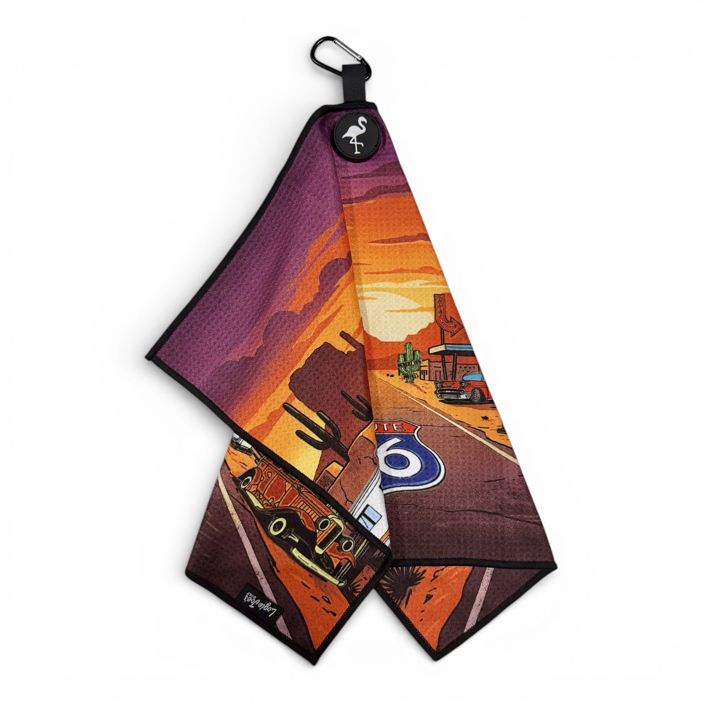 The Route 66 Golf Towel is a premium double-sided microfiber towel (24x16 in) with a desert road design, black border, flamingo logo, carabiner clip, and heavy-duty magnetic attachment for easy use on the course.