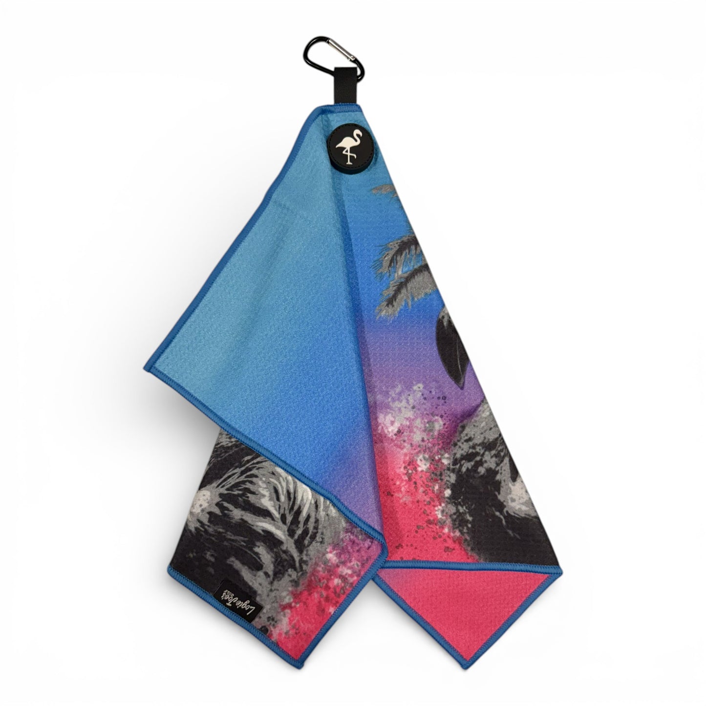 The Flamingo Palm Golf Towel is a 24 x 16 in double-sided microfiber towel with vibrant blue, purple, and pink tropical designs, heavy-duty magnet, carabiner clip, and a black emblem featuring a white flamingo—perfect for any golf enthusiast.