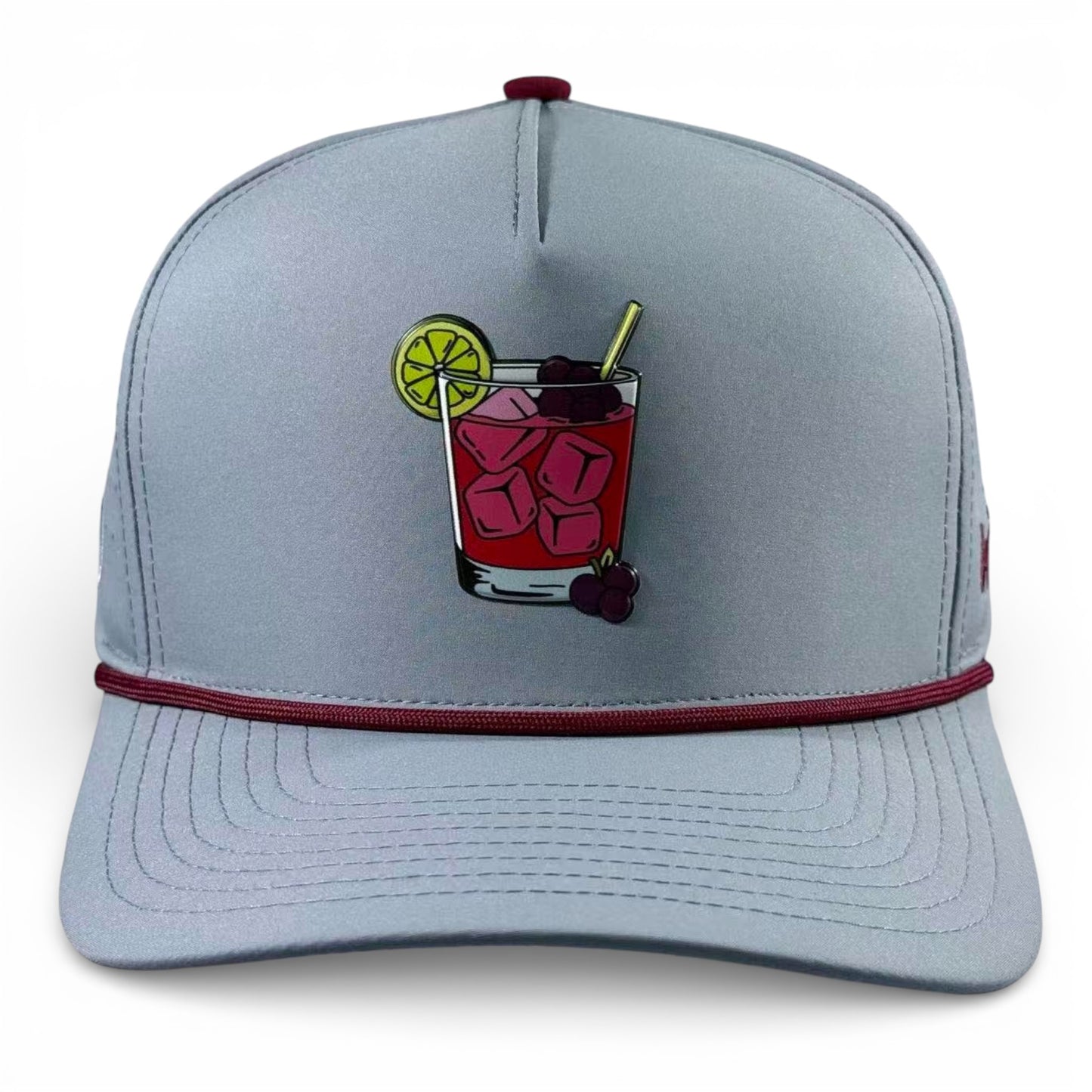 The Transfusion Golf Hat is an adjustable light gray snapback cap with a built-in magnetic ball marker holder and included marker, featuring a front patch of a red cocktail with ice, lime, straw, cherries, and a burgundy bill accent.